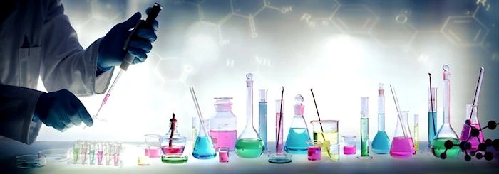 Różnokolorowe próbki w szklanych naczyniach laboratoryjnych na stole; po lewej ręce w rękawiczkach wykonujące pracę pipetą.